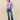 Woman wearing a purple sweater with white sheep patterns and blue jeans on a beige background