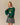 A person wears a forest green Rowing Blazers x Babar Babar Jardinier Cashmere Sweater, featuring an intarsia knit of Babar the Elephant in a yellow cap and red overalls, with BABAR jardinier embroidered above in yellow script.