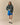 A person wears a forest green Warm & Wonderful Sheep Sherpa Jacket Green over a white shirt, bright blue mesh shorts, white socks, and black mary jane shoes.