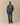 A person wears a forest green Warm & Wonderful Sheep Sherpa Jacket Green with a repeating white sheep pattern, blue jeans, and tan loafers.