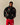 A person wears a black, full-zip Tuxedo Paddington Classic Sherpa Black jacket featuring a repeating Paddington print, paired with red athletic shorts.