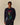 A person wears the Rowing Blazers x Babar Babar in New York Cotton Sweater Navy, featuring a graphic of Babar on the Statue of Liberty, against a plain beige background.