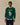 A person wears a green Rowing Blazers x Babar Babar Jardinier Cashmere Sweater, featuring an intarsia design of Babar the elephant holding a red watering can with the text BABAR jardinier above it.