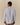 A person with short curly hair is shown from the back, wearing the Paddington Oxford Light Blue Stripe by Rowing Blazers x Paddington™ and brown pants against a plain beige background.
