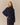 A person wears an oversized navy Kaia Shawl Sweater by Rowing Blazers with a folded shawl collar and a plaid skirt.