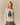 A woman wears an ivory Rowing Blazers x Paddington™ Penelope Paddington Cashmere Sweater featuring the bear in his signature blue coat and red hat.